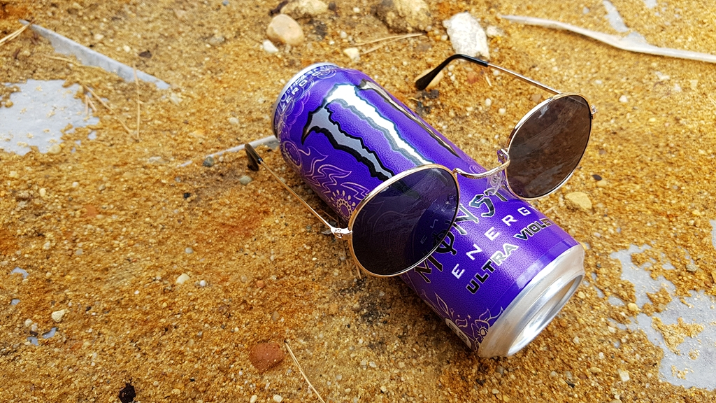 Napój energetyczny Monster Ultra Violet z okularami przeciwsłonecznymi na piasku